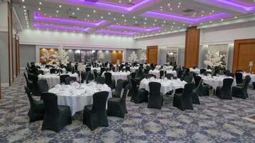 Un salón de banquetes con mesas redondas, sillas negras y manteles blancos.