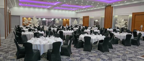 A banquet hall with round tables, black chairs, and white tablecloths.