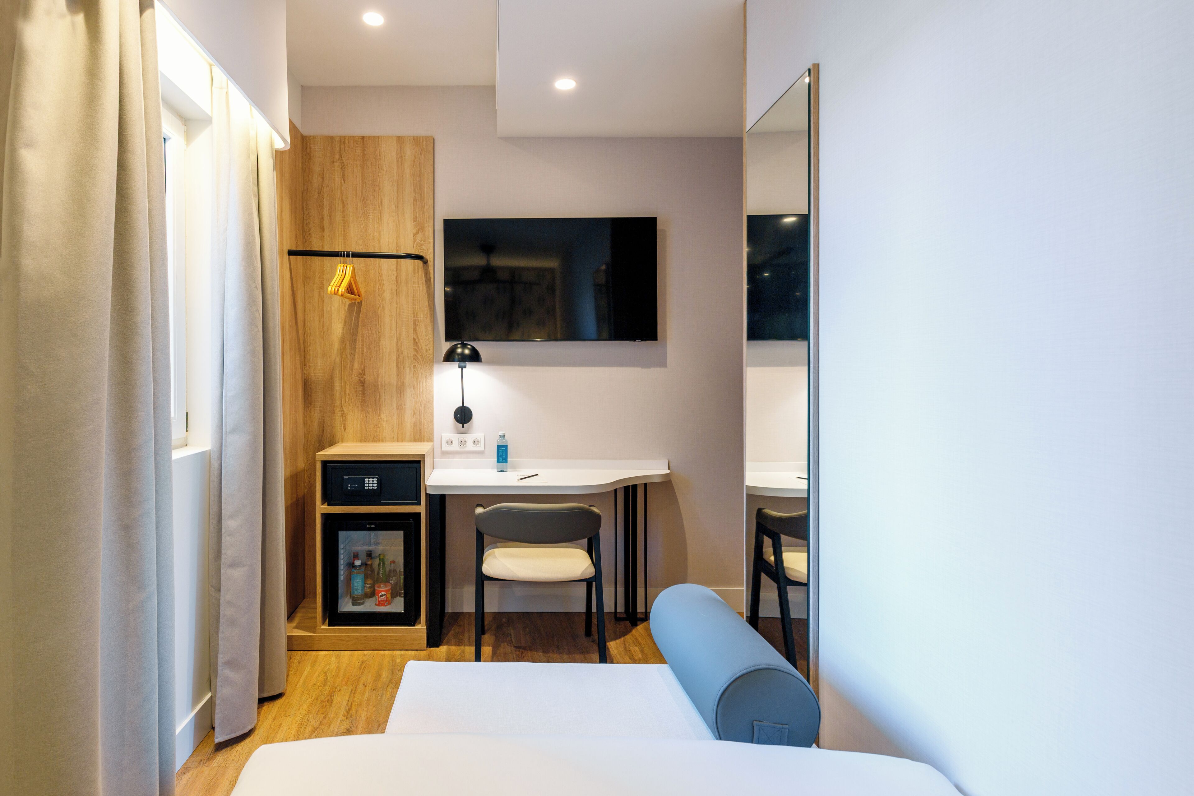 Habitación de hotel con cama, escritorio, silla, mueble bajo y espejo.