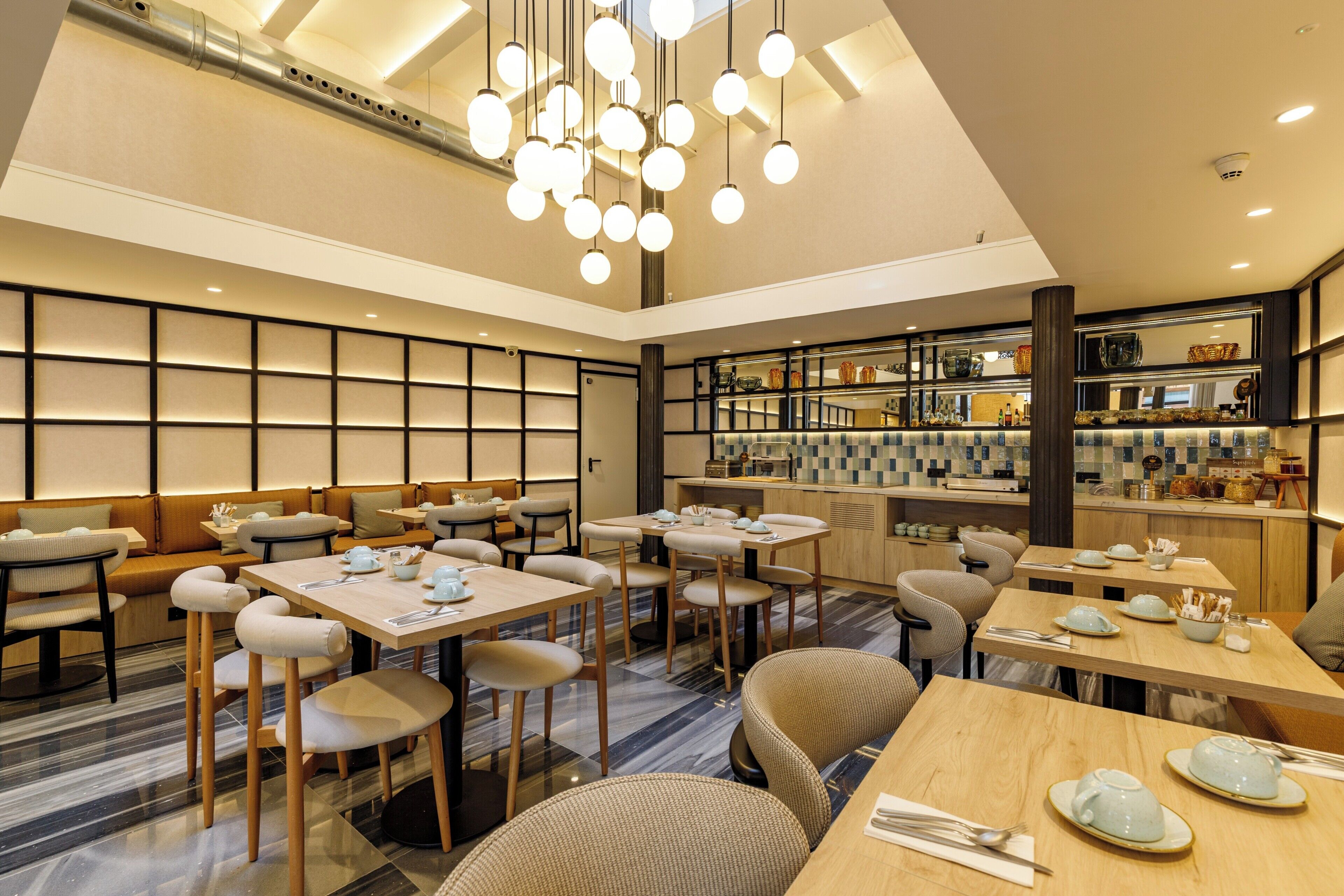 Un restaurante moderno con varias mesas y cabinas, una zona de bar y una cocina al fondo.