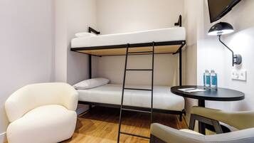 Una cama litera con escalera, un sillón blanco, una mesa redonda con dos botellas y un televisor montado en la pared.