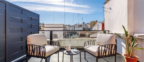 A rooftop terrace with two black metal chairs, a small round table, and a potted plant.