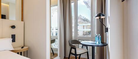 Una habitación de hotel con cama, una mesita de noche con lámpara, una silla y una ventana con cortinas.