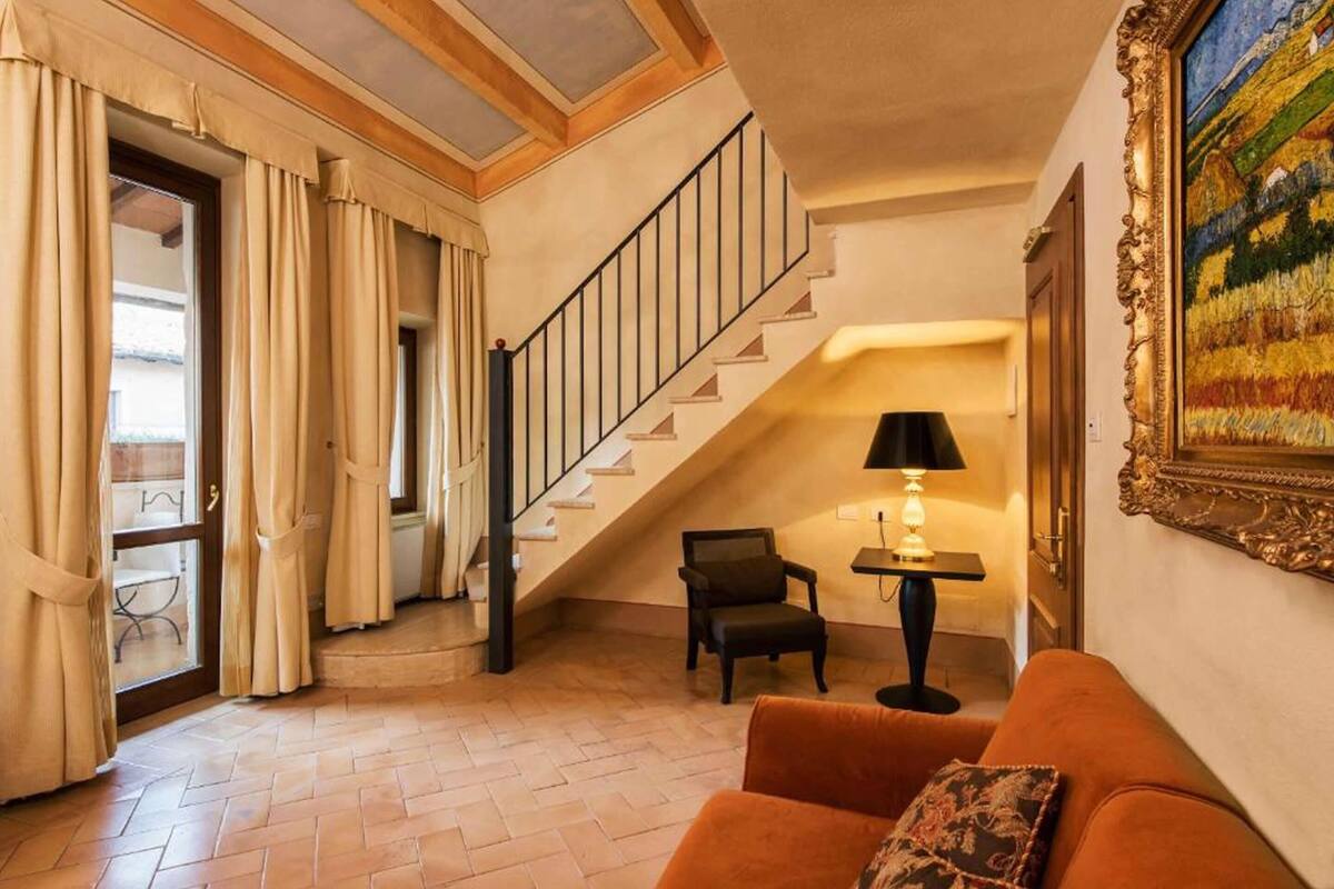 Una sala de estar con una escalera, un sofá, un sillón, una lámpara y un cuadro.