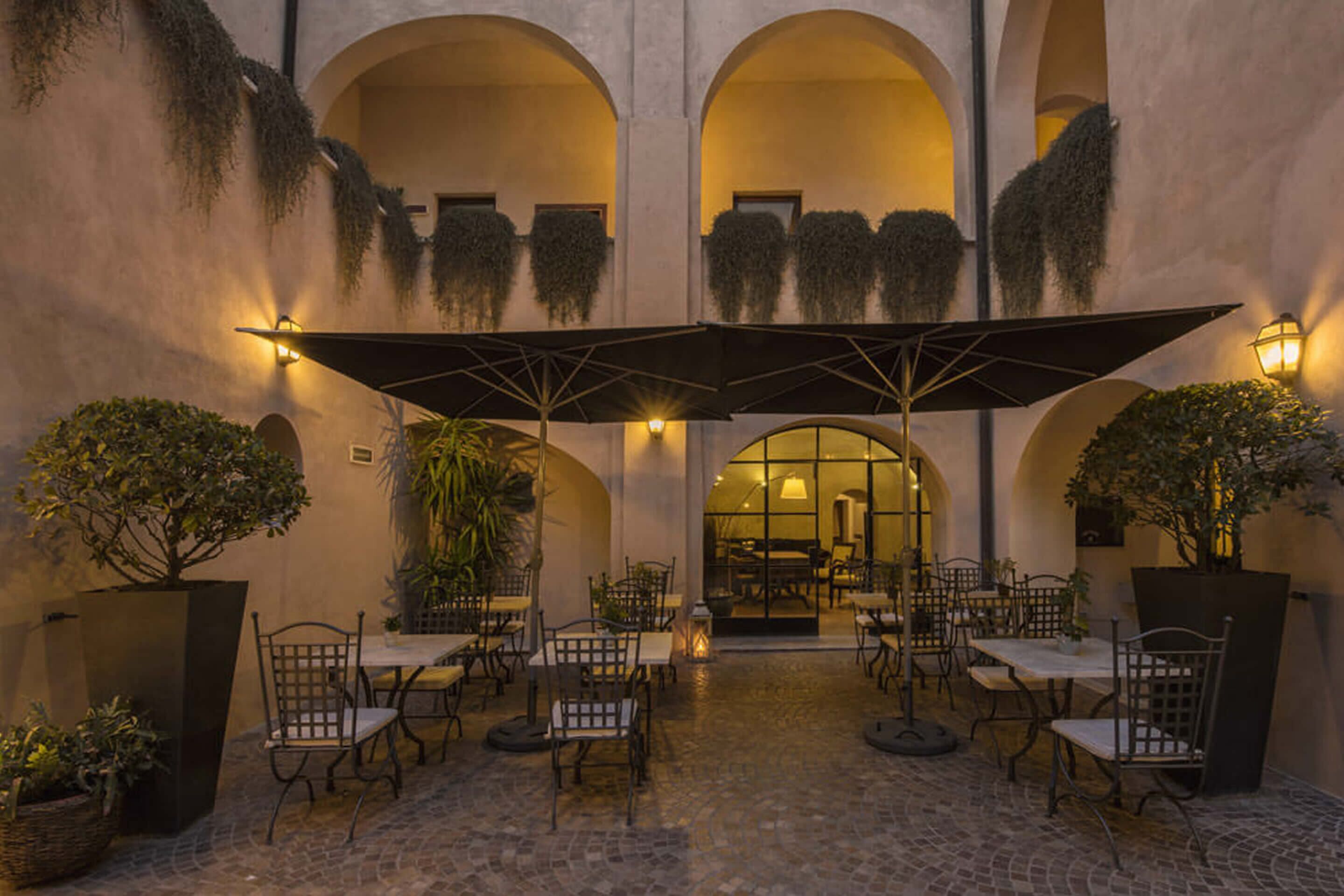 Une terrasse extérieure avec des tables et des chaises, protégée par des parasols et entourée de plantes en pot.