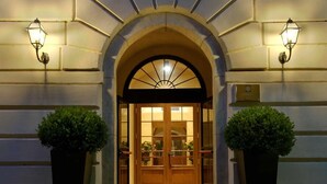 A hotel entrance with a large arched doorway, two potted plants on either side, and wall-mounted lights. - San Biagio Relais (Orbetello)