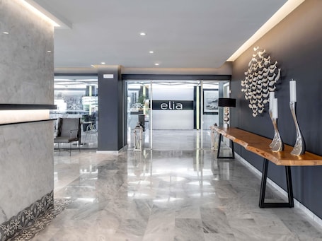 A modern lobby with a marble floor, a reception desk, and a wall-mounted sculpture.