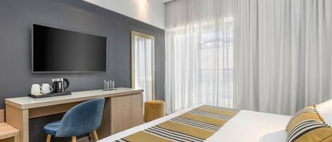 Habitació d'hotel amb un llit, escriptori, cadira, televisió i finestra amb cortines.