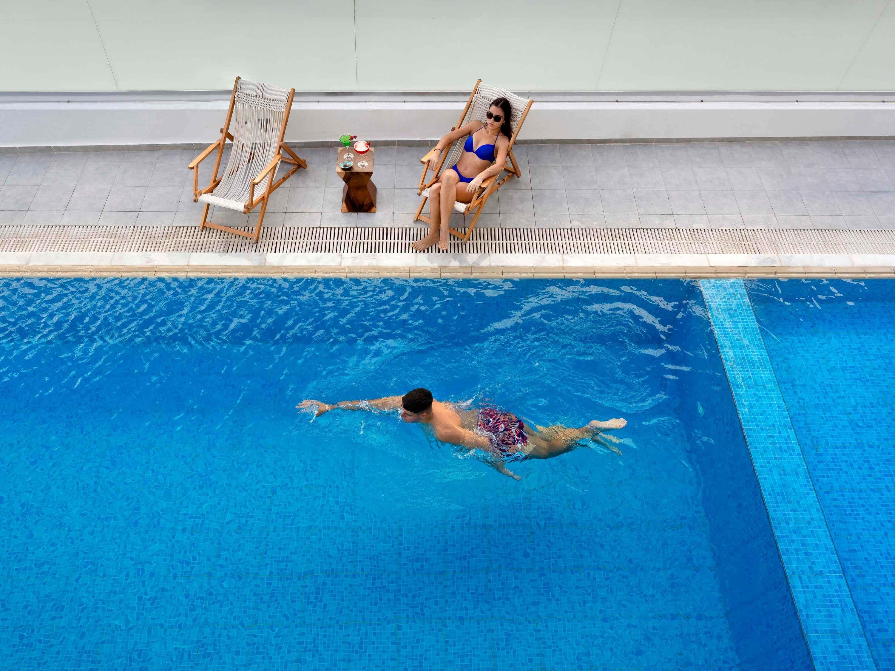 A swimming pool with two lounge chairs and a small table with drinks.