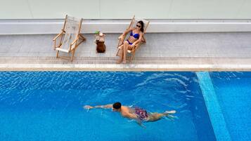 A swimming pool with two lounge chairs and a small table with drinks.