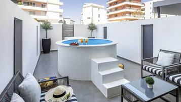 A rooftop terrace with a hot tub, outdoor seating, and a view of surrounding buildings.