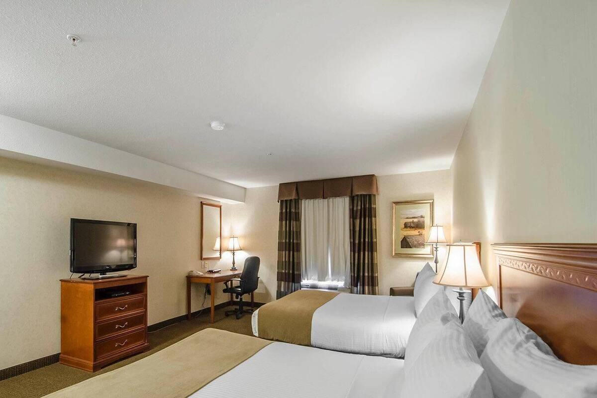 A hotel room with two beds, a desk with a chair, a television, and a window with curtains.