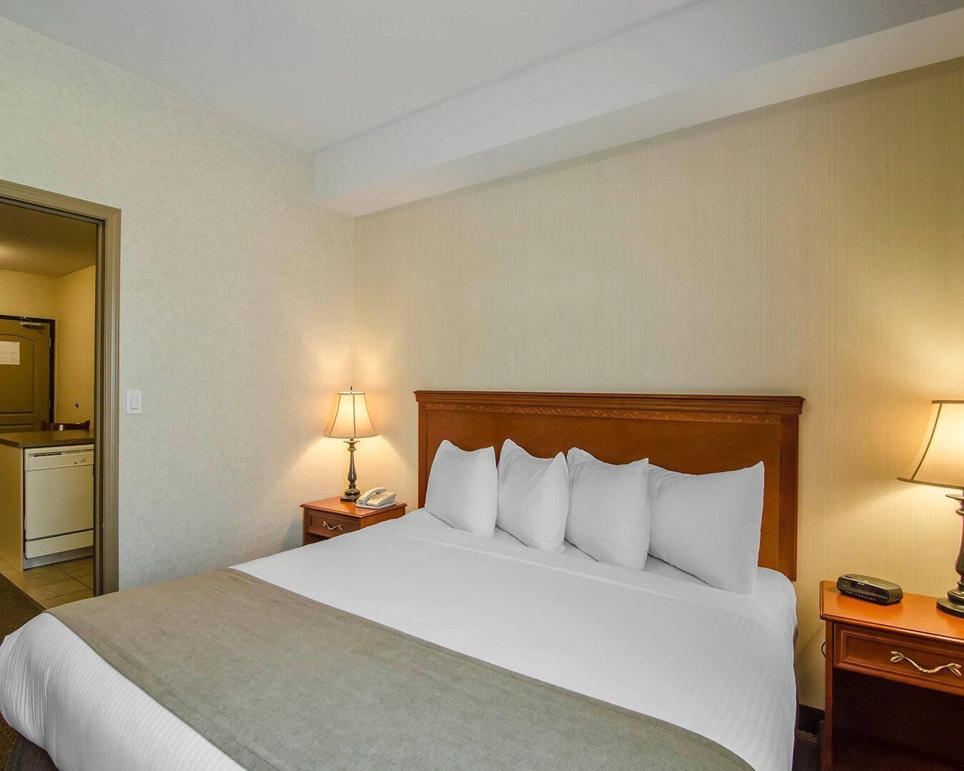 A hotel room with a bed, a nightstand with a lamp, a bedside table with a phone, and a mirror on the wall.