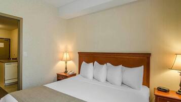 A hotel room with a bed, a nightstand with a lamp, a bedside table with a phone, and a mirror on the wall.