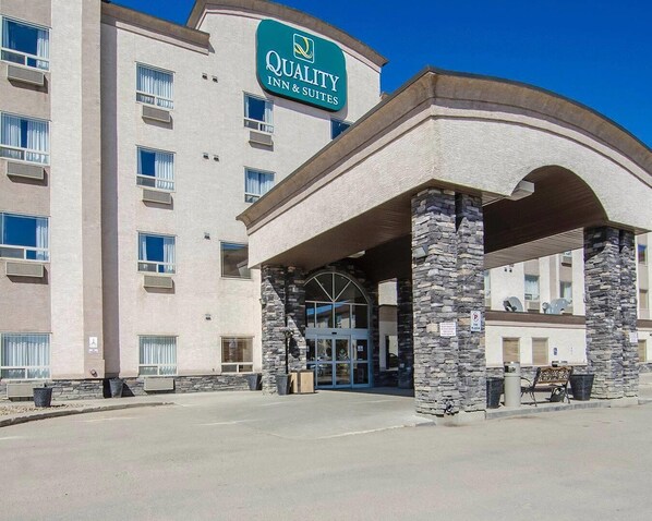 A hotel with a sign reading 'Quality Inn & Suites,' featuring a stone facade, a covered entrance, and a clear blue sky.