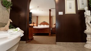 A bathroom with a bathtub, a wooden bed with a canopy, and a statue. - Quality Inn & Suites (Grande Prairie)