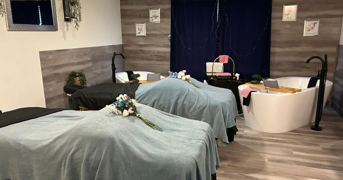 A spa room with two beds, a bathtub, and a small table with a laptop.