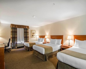A hotel room with three beds, a desk, a chair, a window with curtains, and a wall-mounted picture. - Quality Inn & Suites (Grande Prairie)