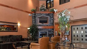 A lobby with a stone fireplace, leather sofas, a TV, and a large potted plant. - Quality Inn & Suites (Grande Prairie)