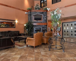 A lobby with a stone fireplace, leather sofas, a TV, and a large potted plant.