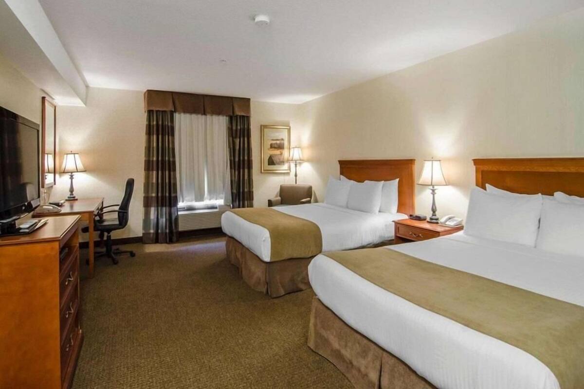 A hotel room with two beds, a desk, a chair, a TV, and a window with curtains.