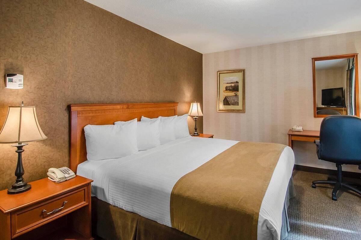 A hotel room with a bed, bedside lamps, a desk with a chair, a telephone, a painting, and a mirror.