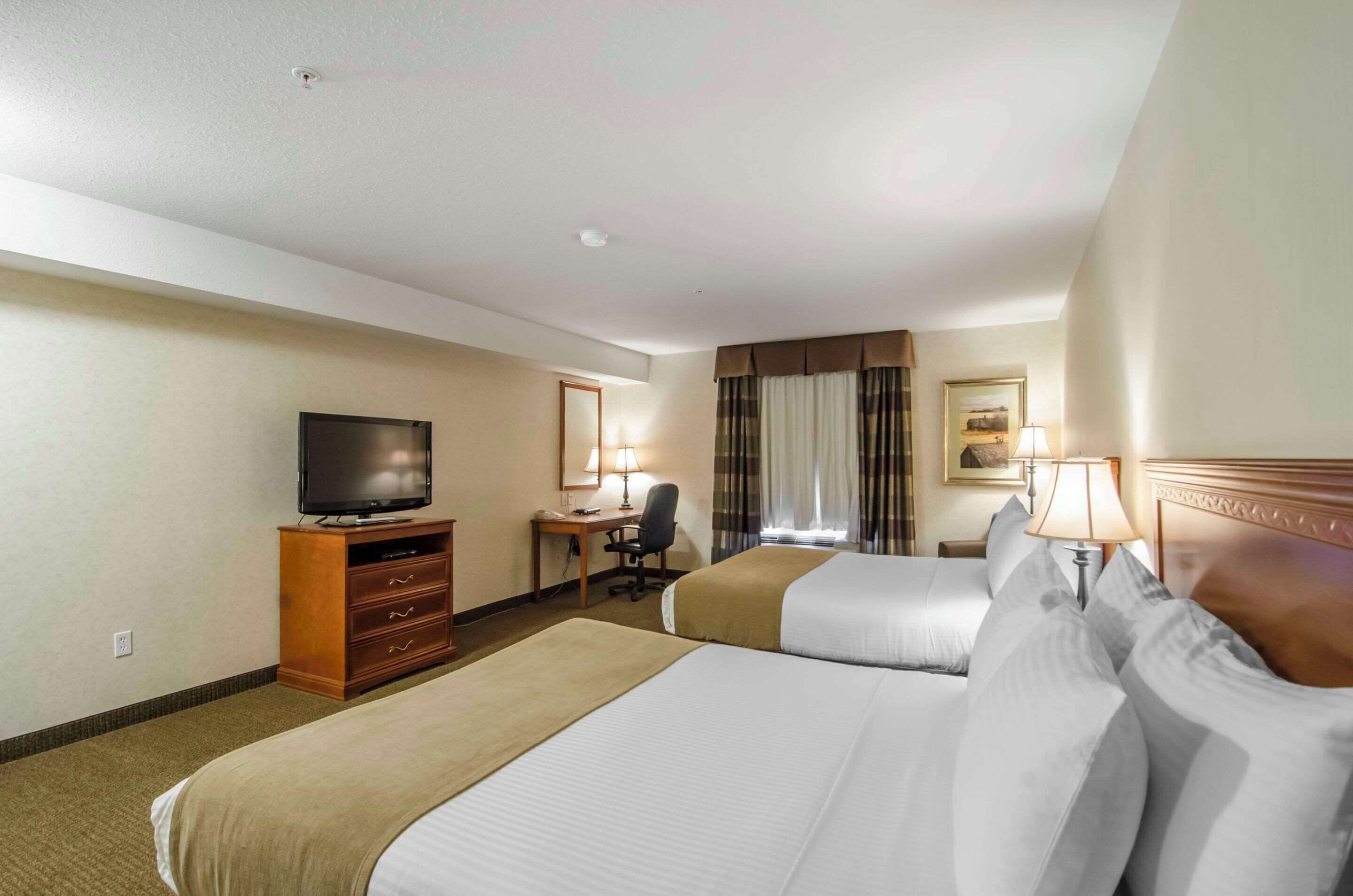 A hotel room with two beds, a desk with a chair, a television, and a lamp.