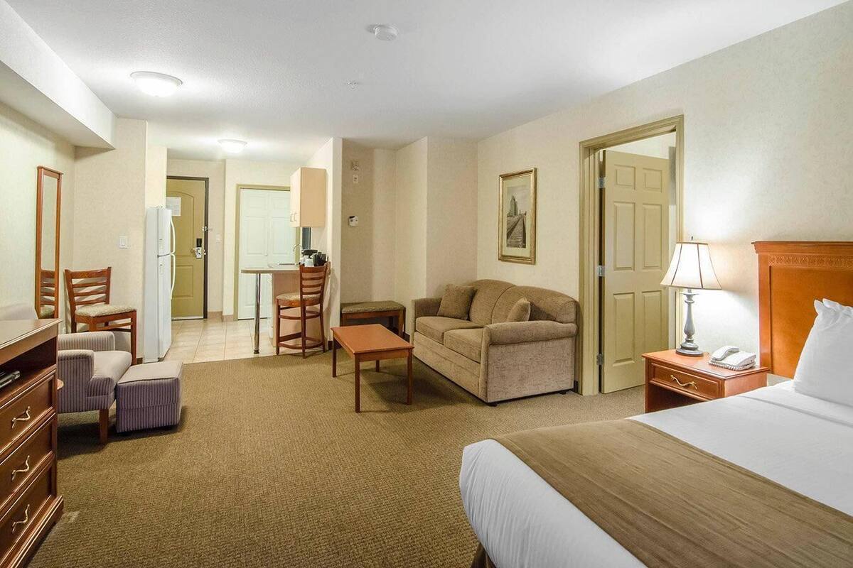 A hotel room with a bed, a sofa, a desk, a chair, a lamp, and a dresser.