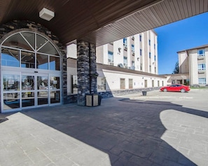 A hotel entrance with a stone facade, a covered entrance area, and a red car parked outside. - Quality Inn & Suites (Grande Prairie)