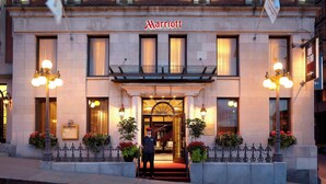 Entrada de un hotel Marriott con una fachada imponente, una alfombra roja y un guardia de seguridad en la entrada.
