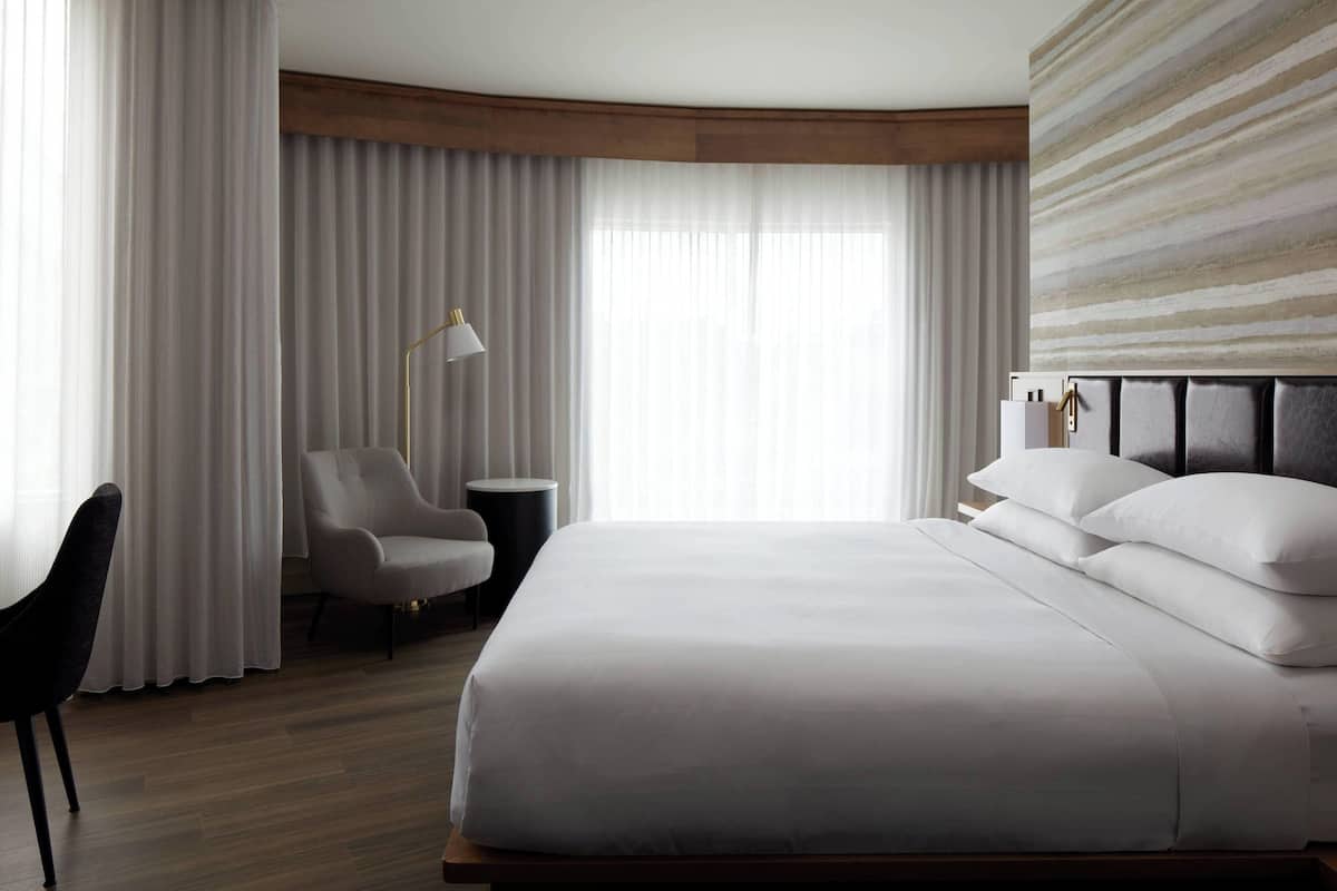 A hotel room with a large bed, a chair, a desk, and a lamp.