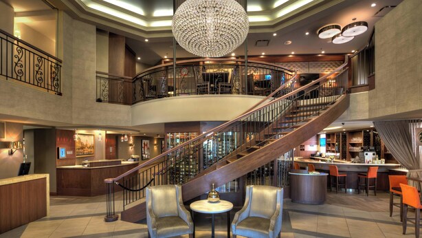 Un vestíbulo amplio con una gran escalera, una zona de recepción y un bar-salón.