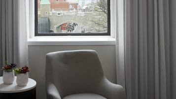 Una habitación con vista a un paisaje urbano a través de una ventana, un sillón gris, una mesita con plantas en macetas y una mesita auxiliar negra.