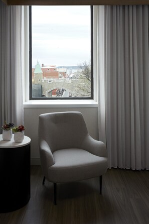 A room with a view of a cityscape through a window, a grey armchair, a small table with potted plants, and a black side table. - Quebec City Marriott Downtown (Québec City)