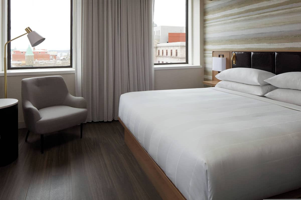 A hotel room with a large bed, a chair, a desk, and a lamp.