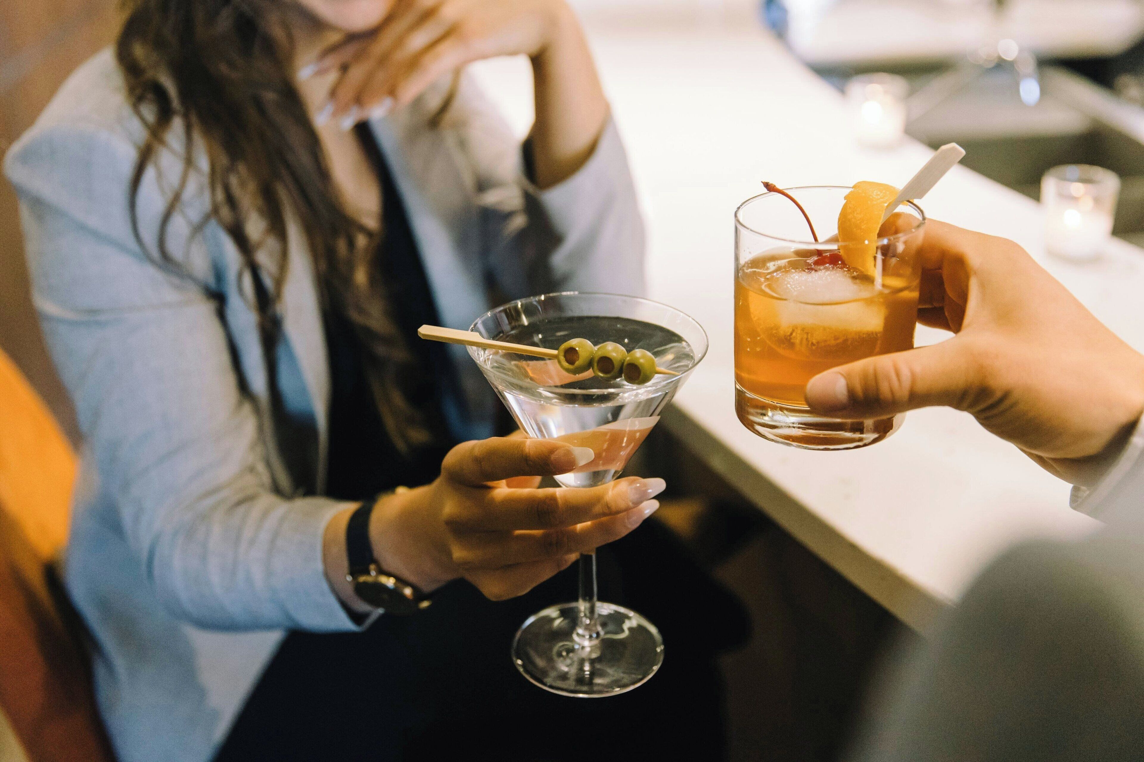 Two people holding martini glasses with olives and a lemon slice garnish.