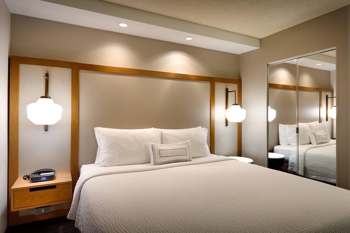 Quarto de hotel com cama grande, mesas de cabeceira, espelho e luminárias na parede.