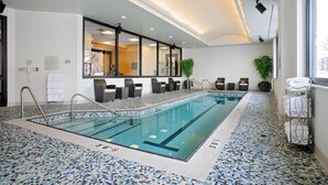 A large indoor swimming pool with clear water, tiled flooring, and a seating area with chairs and a plant. - Hilton Garden Inn Portland Downtown Waterfront (Portland)