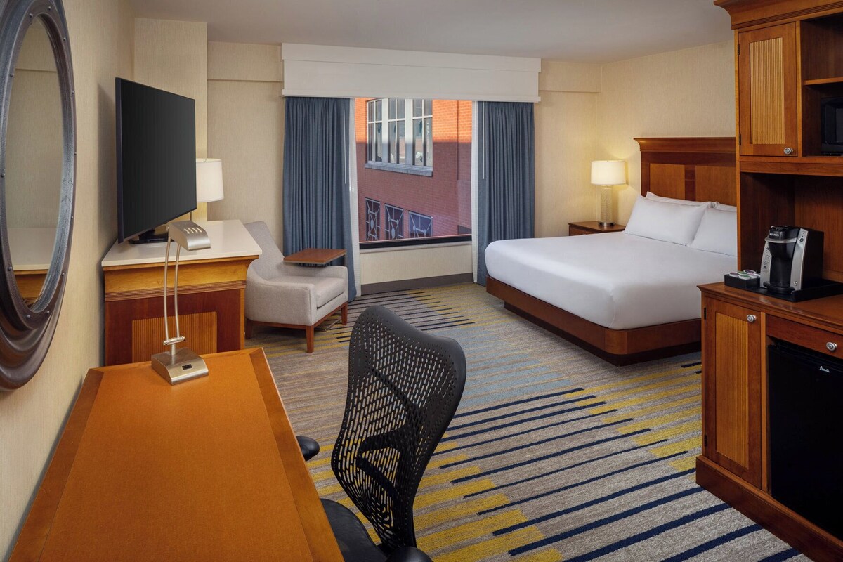 A hotel room with a bed, desk, chair, TV, and a coffee maker.