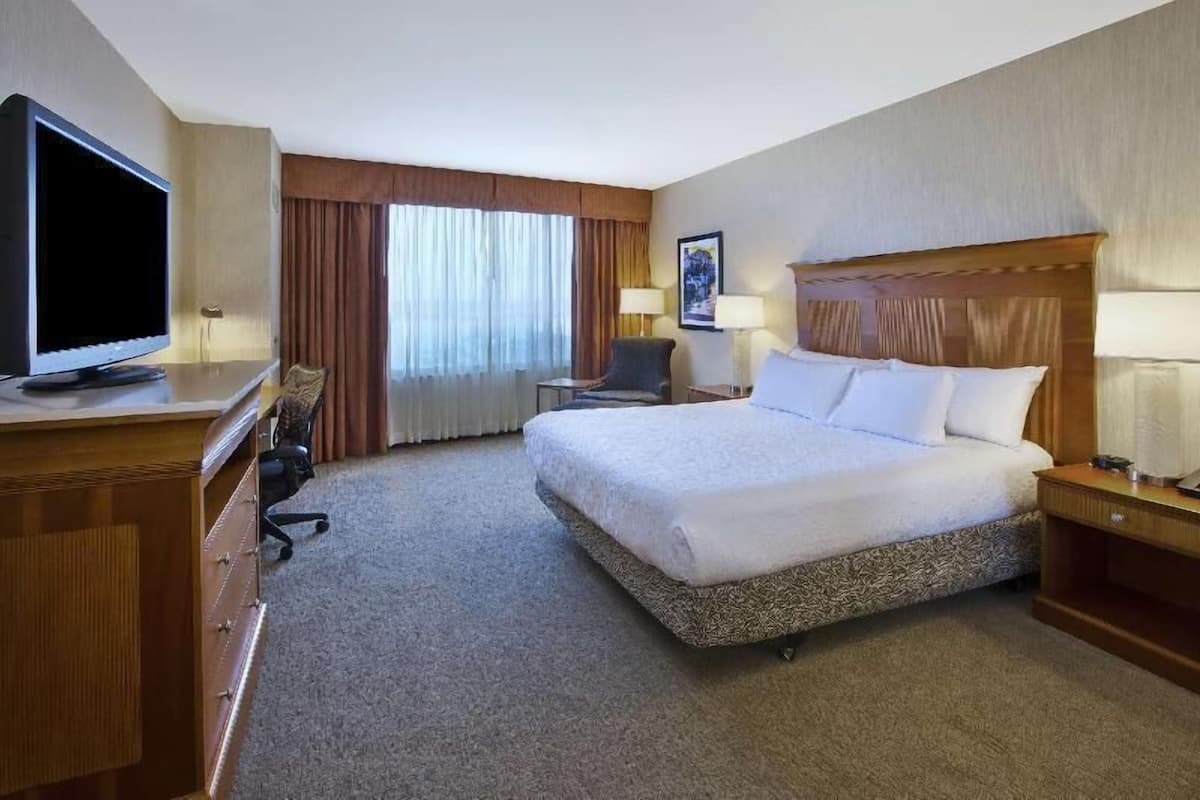 A hotel room with a bed, a desk, a television, and a window with curtains.