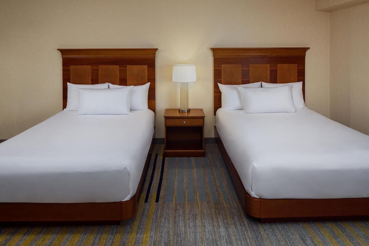 A hotel room with two single beds, a nightstand with a lamp, and a striped carpet.