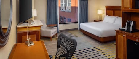 Habitación de hotel con cama, escritorio, silla, televisor y vista a un edificio por la ventana.