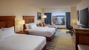 A hotel room with two beds, a desk, a TV, and a view of a body of water. - Hilton Garden Inn Portland Downtown Waterfront (Portland)
