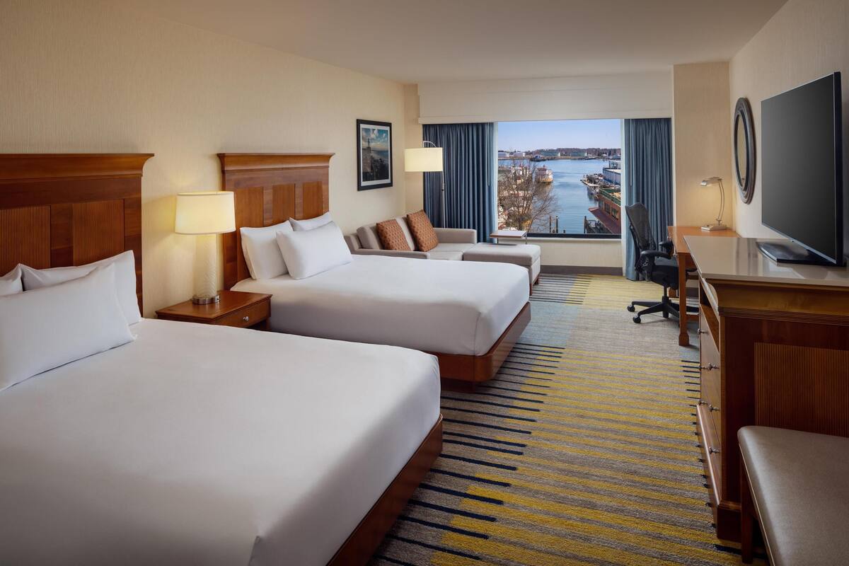 A hotel room with two beds, a desk, a TV, and a view of a body of water.