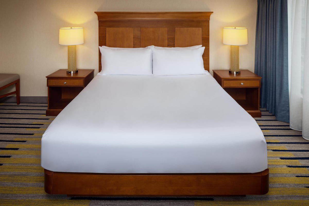 A large bed with white linens, two bedside tables with lamps, and a wooden headboard.