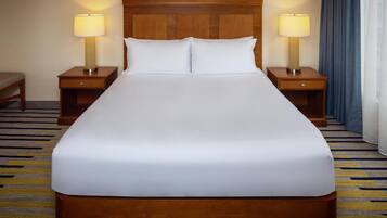 A large bed with white linens, two bedside tables with lamps, and a wooden headboard.