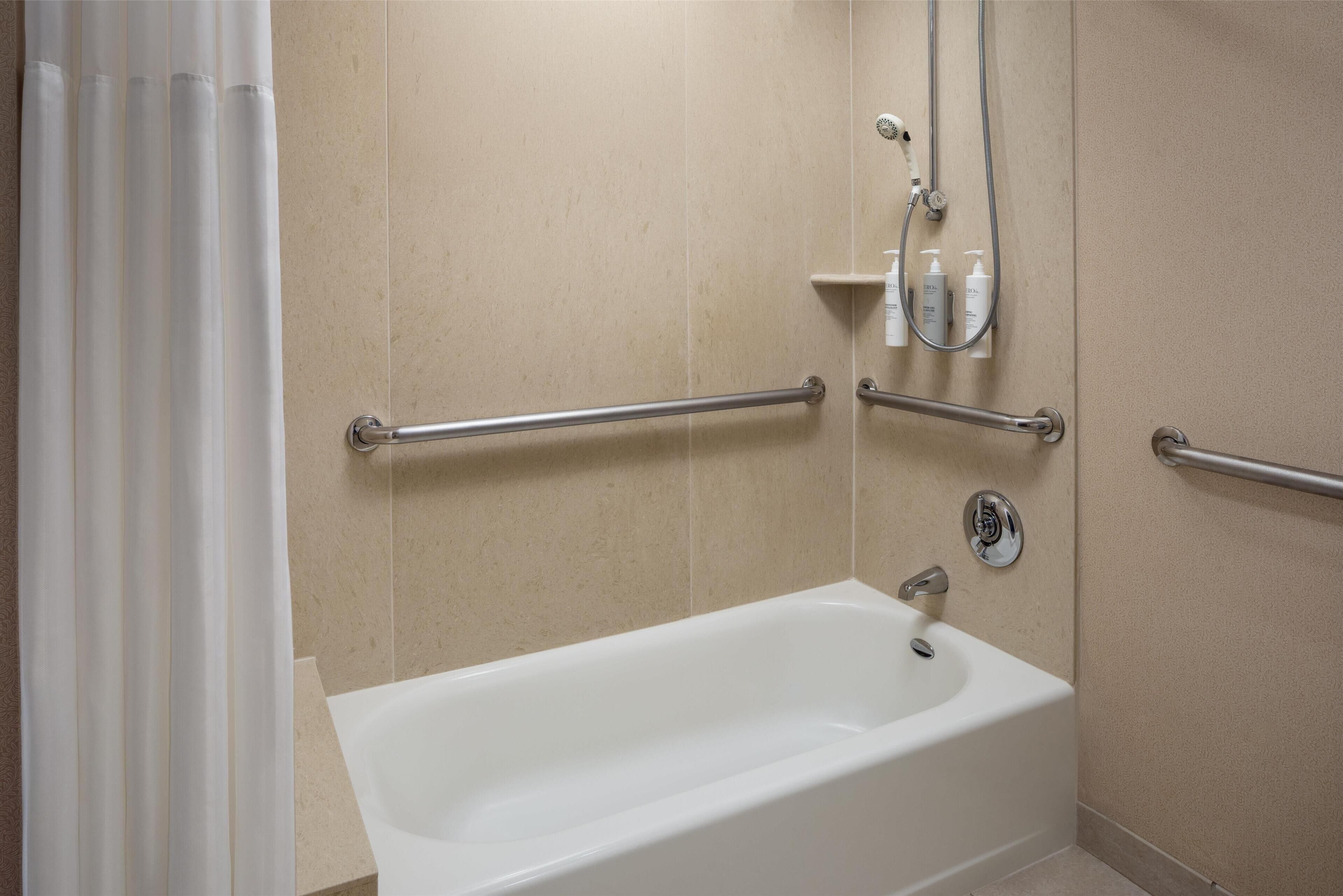 A bathroom with a bathtub, grab bars, and a showerhead.