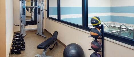 Un gimnasio con equipamiento de ejercicio, una banca y un estante con balones deportivos.