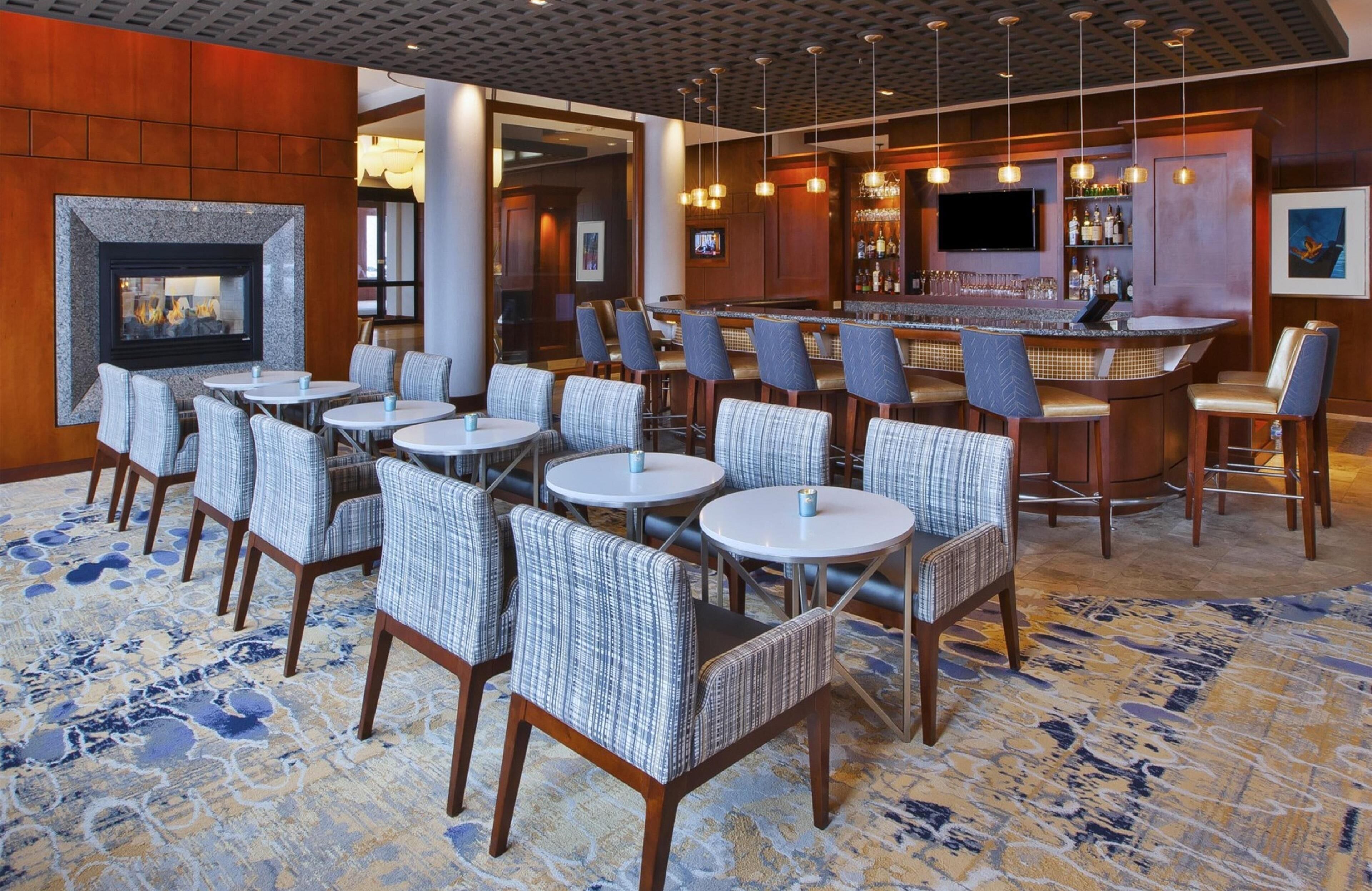 Un vestíbulo de hotel con zona de bar, arreglos de asientos y chimenea.