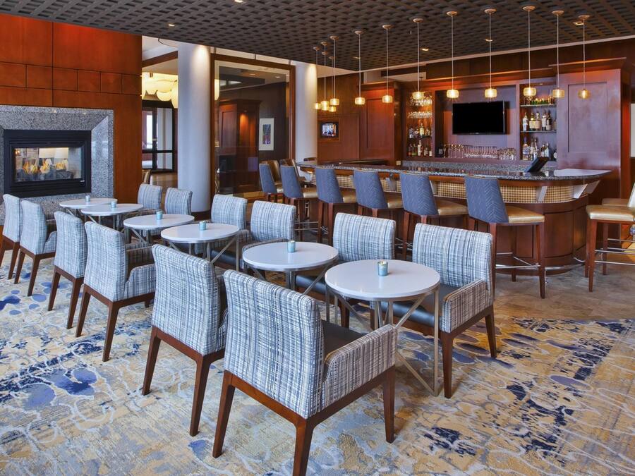Un vestíbulo de hotel con zona de bar, arreglos de asientos y chimenea.